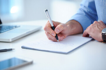 Close up of Business Professional Writing on Paper in Office Setting with Laptop and Smartphone Documenting Work Tasks