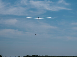 White glider aircraft soaring through blue sky with white clouds on clear day