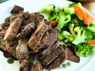 Grilled beef steak served with steamed carrots and broccoli on a plate.
