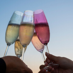 Champagne flutes are raised in a toast as friends gather at sunset, enjoying sparkling drinks and each other's company against a vibrant evening sky.