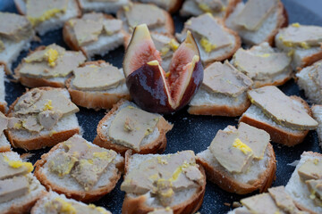 A beautiful arrangement of toasted bread topped with foie gras and garnished with fig, all displayed elegantly for guests at a midday outdoor gathering.