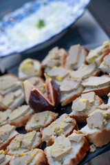 A beautiful arrangement of toasted bread topped with foie gras and garnished with fig, all displayed elegantly for guests at a midday outdoor gathering.