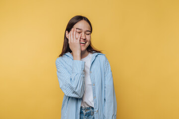 Fototapeta premium A young woman in a striped shirt laughing with her hand on her face against a yellow background.