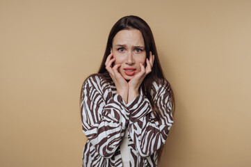 A worried woman with long hair in a zebra-patterned shirt against a beige background.