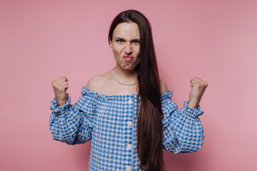 A woman in a blue checkered off-shoulder top expressing anger with clenched fists against a pink...