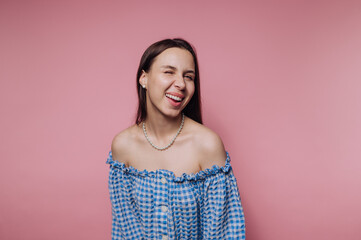 Young woman in blue checkered off-shoulder top laughing against pink background.