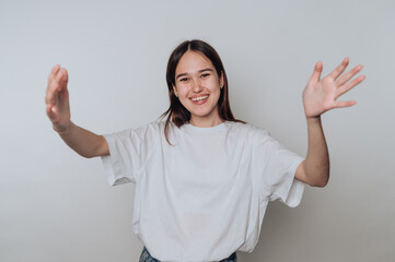 A young woman in a white t-shirt smiling with arms outstretched against a plain background.