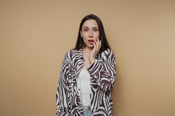 A surprised woman with long dark hair wearing a zebra-patterned shirt against a beige background.