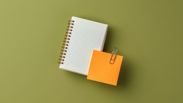 Spiral notebook with orange sticky note and paperclip on green