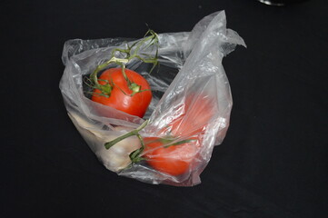 Tomatoes in thin translucent plastic bag, black background, separated, negative space, copy space,