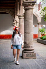 A smiling Latina woman in catrina Day of the Dead makeup and a flower crown walks through a...