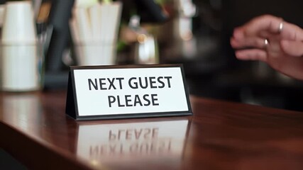 Welcoming Hand Flipping Next Guest Please Sign on Glossy Wooden Counter A Customer Service Invitation in Restaurant Setting Promotes Immediate Assistance in Warm Interior for Adobe Stock Photos