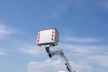 A hydraulic lift is raised high, showcasing its platform against a bright blue sky with scattered...