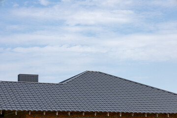 Modern building's roof showcases intricate gray tiles set against a bright blue sky with fluffy...