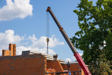 A construction crane is positioned at a building site, lifting materials against a backdrop of...