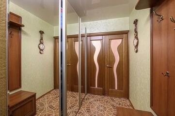 well-lit entryway with wooden doors, patterned floor tiles, and light green patterned walls....
