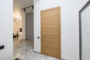 Modern interior with a wooden door, marble floor, white walls, and a glimpse into a living room