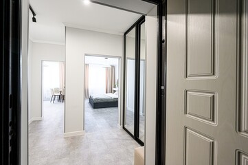Interior shot showcasing an open doorway leading into a modern apartment. Neutral tones with views into the living and bedroom areas