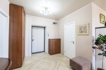 bright entryway with a wooden wardrobe, beige tile floor, and white doors. Art adorns the walls