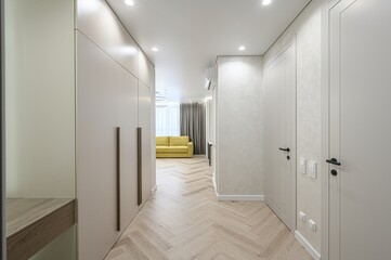 Modern interior featuring a hallway with light wood herringbone flooring, beige built-in wardrobes,...