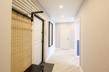 well-lit hallway with light walls, wooden floors, and multiple doors. A bamboo screen is near the...