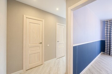 Hallway with wooden doors, light walls, and light wood flooring. A room with two-tone walls is seen through a doorway