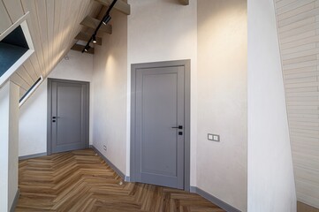 modern interior hallway with two gray doors, herringbone wood floors, light walls, and a unique ceiling design