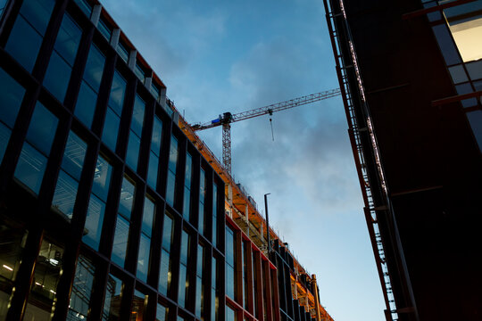 Modern building construction in Dublin with tower crane against evening sky. Contemporary architecture development with glass facade and construction equipment.