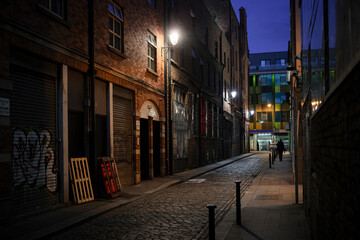 Narrow cobblestone street in Dublin at dusk with Victorian brick buildings and warm street lighting. Historic Irish city laneway with atmospheric evening ambiance.