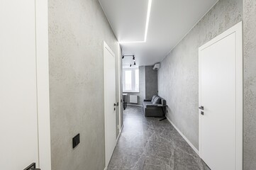 modern hallway with textured gray walls, marble floors, and white doors. A gray sofa and table are...