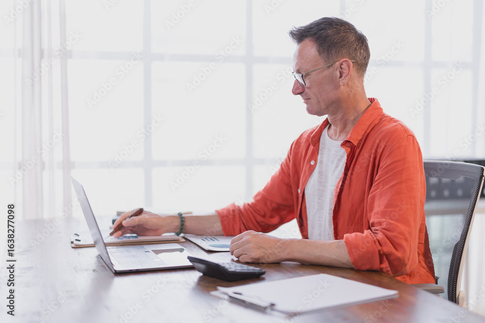 Poster focused mature businessman in casual clothes working with laptop and analyzing graphs and charts at 