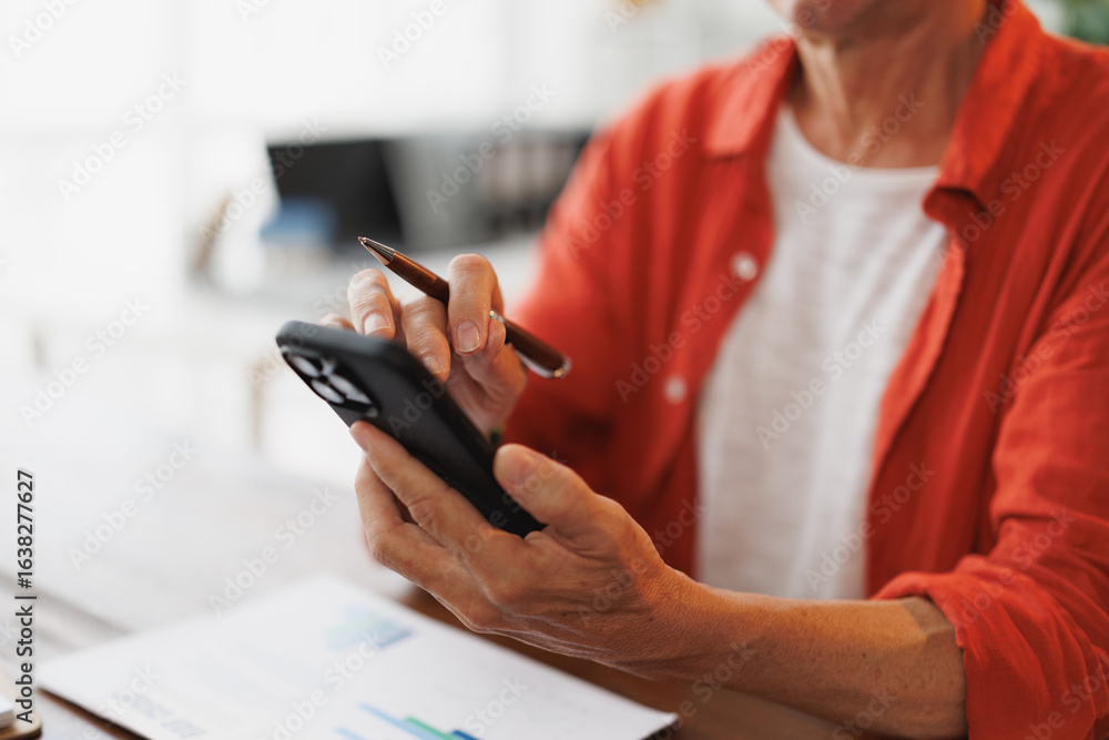 Poster close-up of a senior manager using smartphone and taking notes with a pen while analyzing financial 