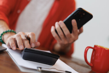 Senior woman using calculator and checking data on smartphone while calculating home finances, managing domestic bills and making payments online