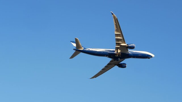 Commercial airplane in low flight against a clear blue sky, viewed from below at an angle, with landing gear extended during ascent or approach. Taking off, altitude gain, flying over, airport. 