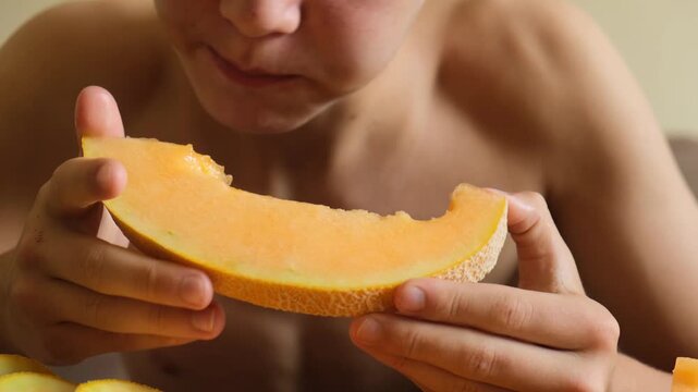 Very hungry teenage boy holding a slice of ripe yellow melon greedily bites and eats juicy fruit pulp. Melon juice runs down the boy's hands. Eating fruits helps the body grow and stay healthy.