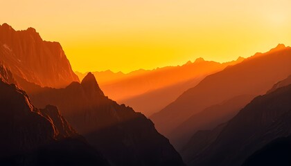 Naklejka premium Golden sunset illuminates a dramatic mountain range, casting long shadows across deep valleys.