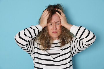 Woman suffering from hangover on light blue background