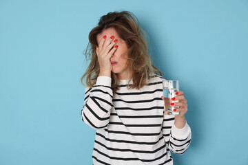 Woman with glass of water suffering from hangover on light blue background