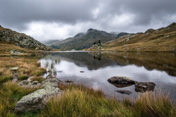 Calm alpine lake reflecting mountains under a cloudy sky