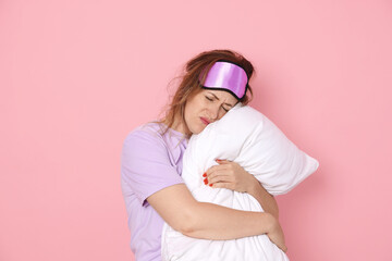 Woman with pillow suffering from hangover on pink background