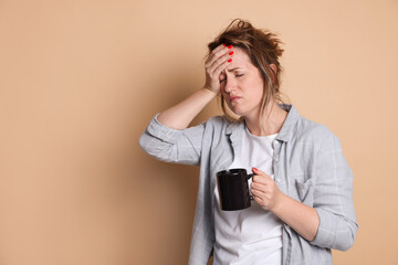 Woman with cup of coffee suffering from hangover on beige background. Space for text