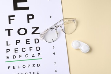Vision test chart, glasses and lenses on beige background, above view