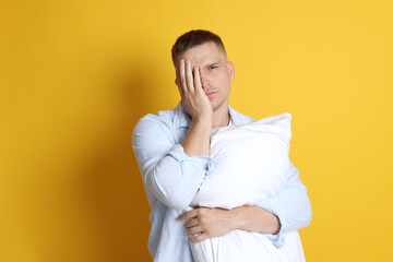 Man with pillow suffering from hangover on orange background