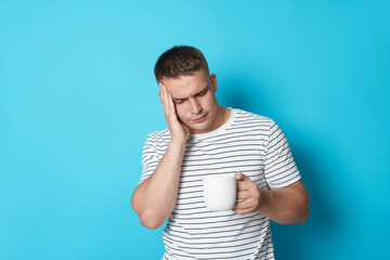 Man with cup of drink suffering from hangover on light blue background
