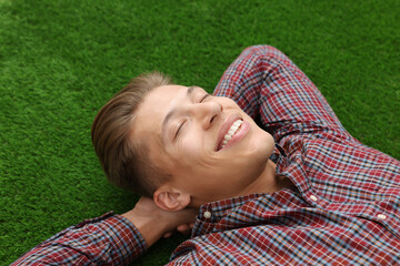 Dream come true. Positive young man thinking about something while lying on green grass