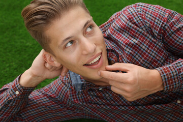 Dream come true. Positive young man thinking about something while lying on green grass