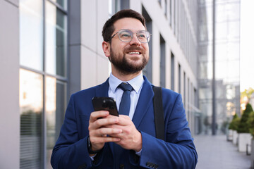 Successful businessman with smartphone near office building