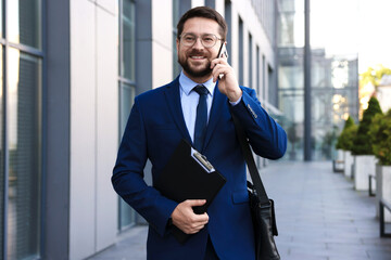 Successful businessman talking on phone near office building