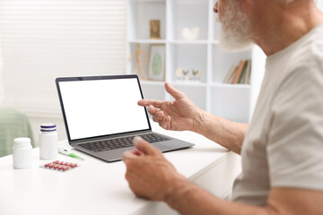 Senior man having online consultation with doctor via laptop at table indoors, closeup