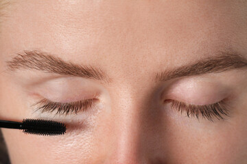 Naklejka premium Young woman applying mascara onto her eyelashes, closeup
